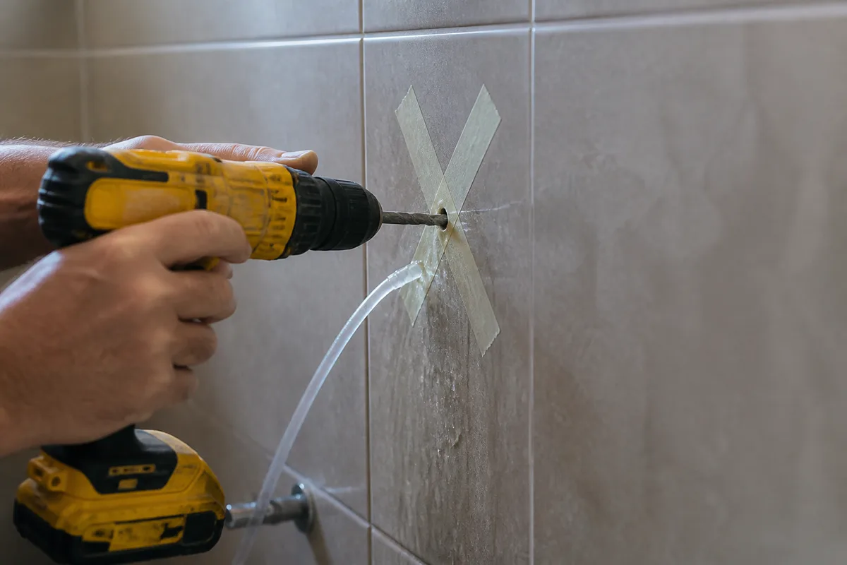 Perceuse équipée d’un foret diamanté sur un carreau de salle de bains avec ruban adhésif et refroidissement à l’eau