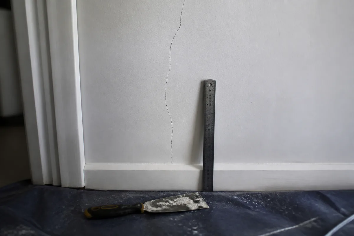 Fissure sur un mur intérieur en plâtre observée avec une règle et un couteau à enduire