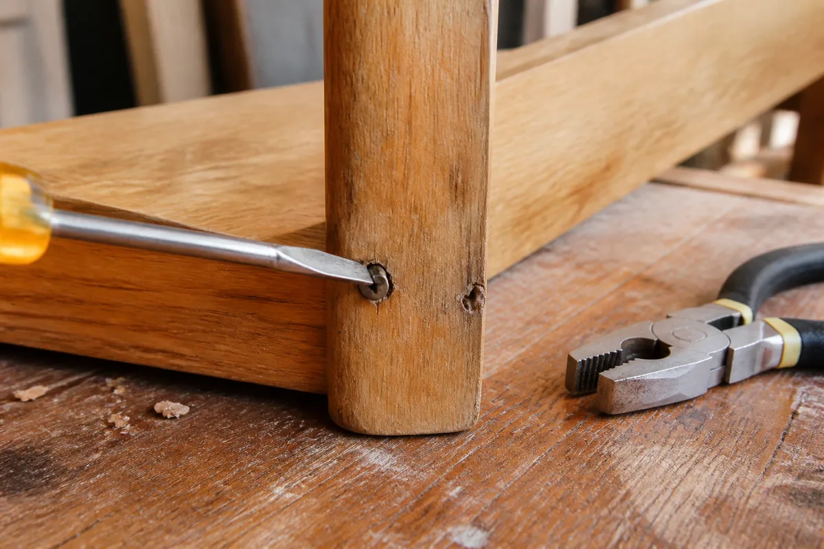 Retirer une vis qui tourne dans le vide avec un tournevis plat et une pince sur une pièce en bois
